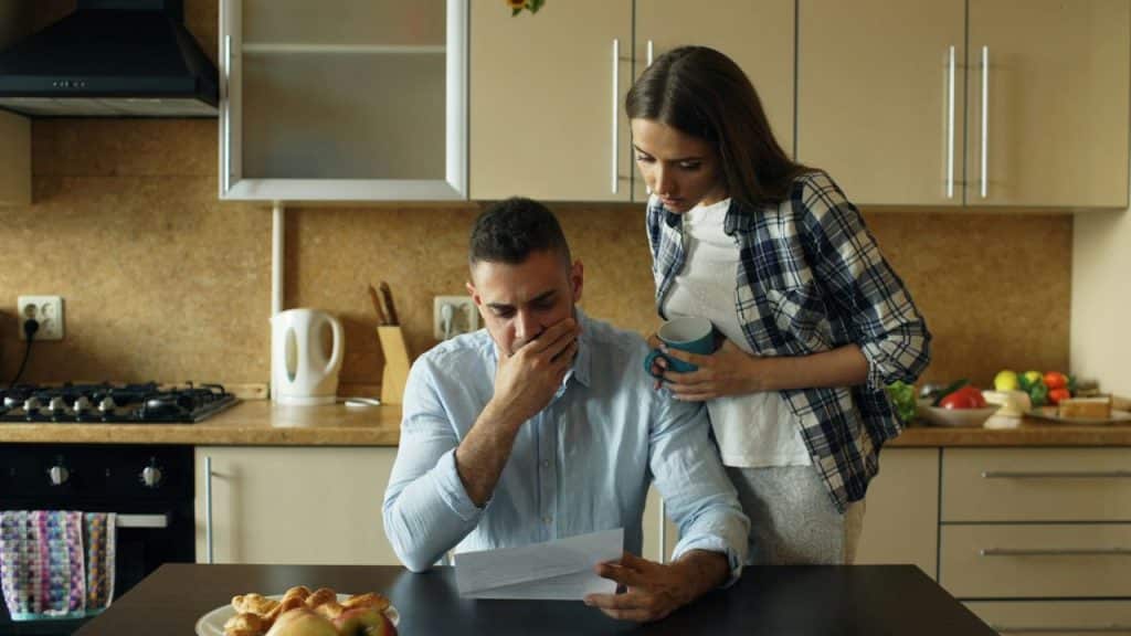 A man and woman looking at a document together in a kitchen with breakfast food.