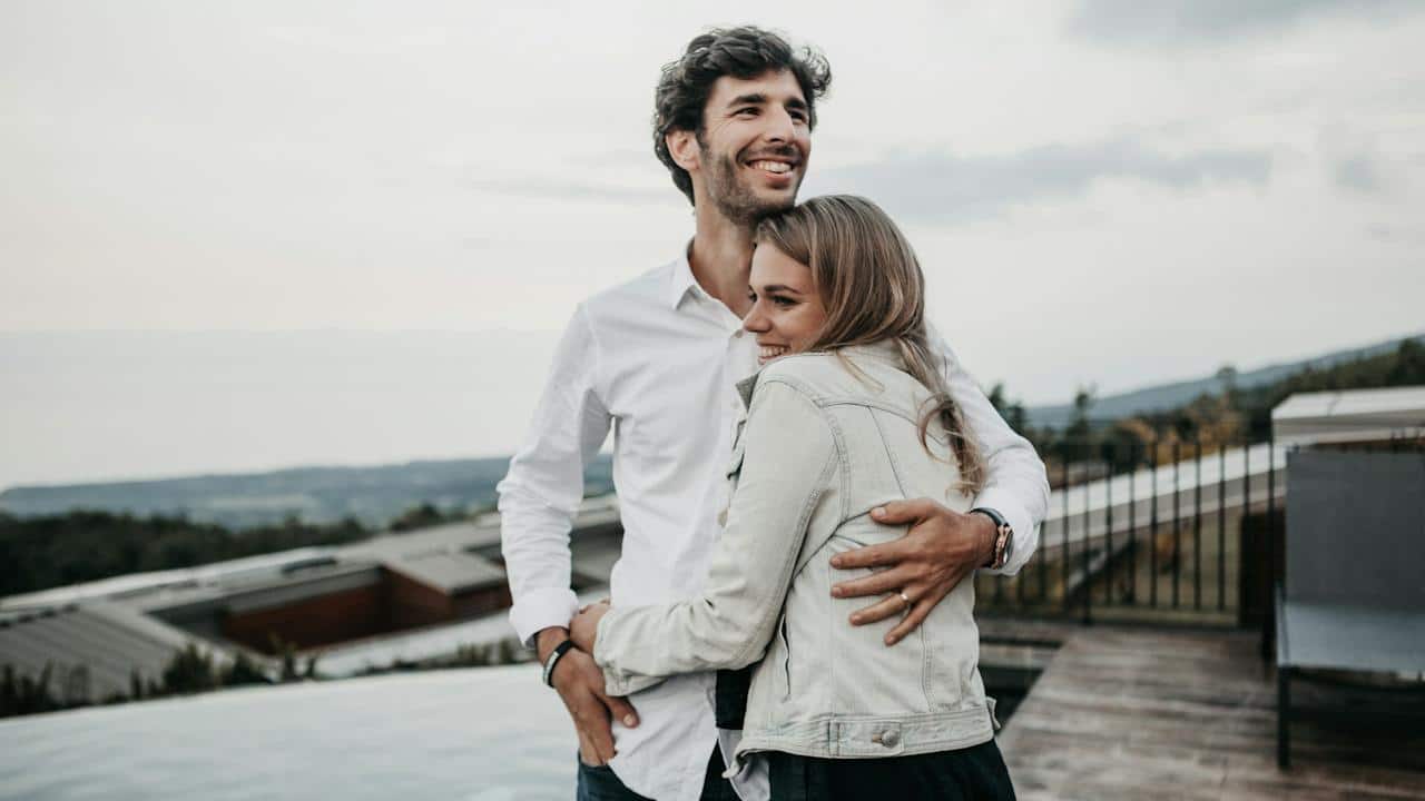A smiling couple hugging each other while standing on the top of a building.