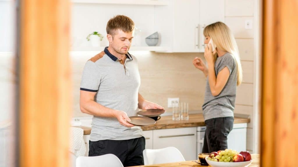 A man holds two plates in a kitchen while a woman talks on her phone.