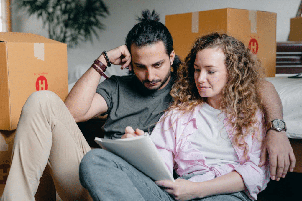Pensive couple looking through notebook while sitting near boxes