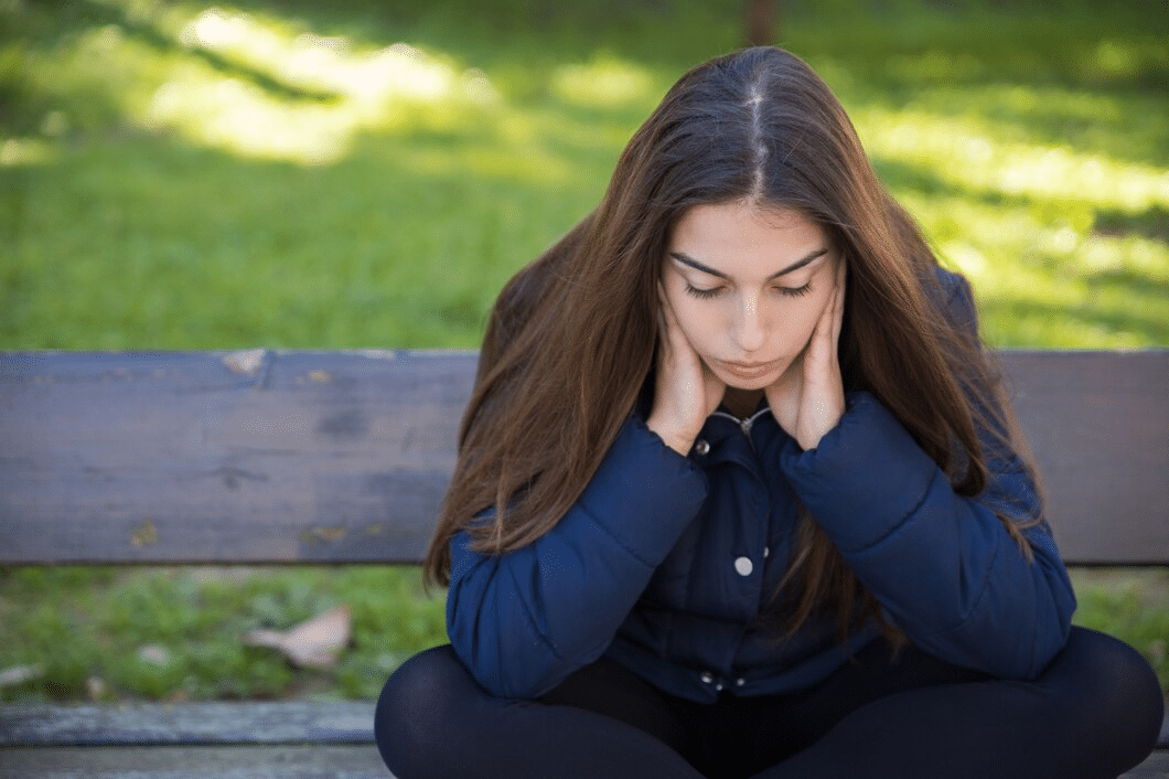 Pensive woman sitting on bench in park