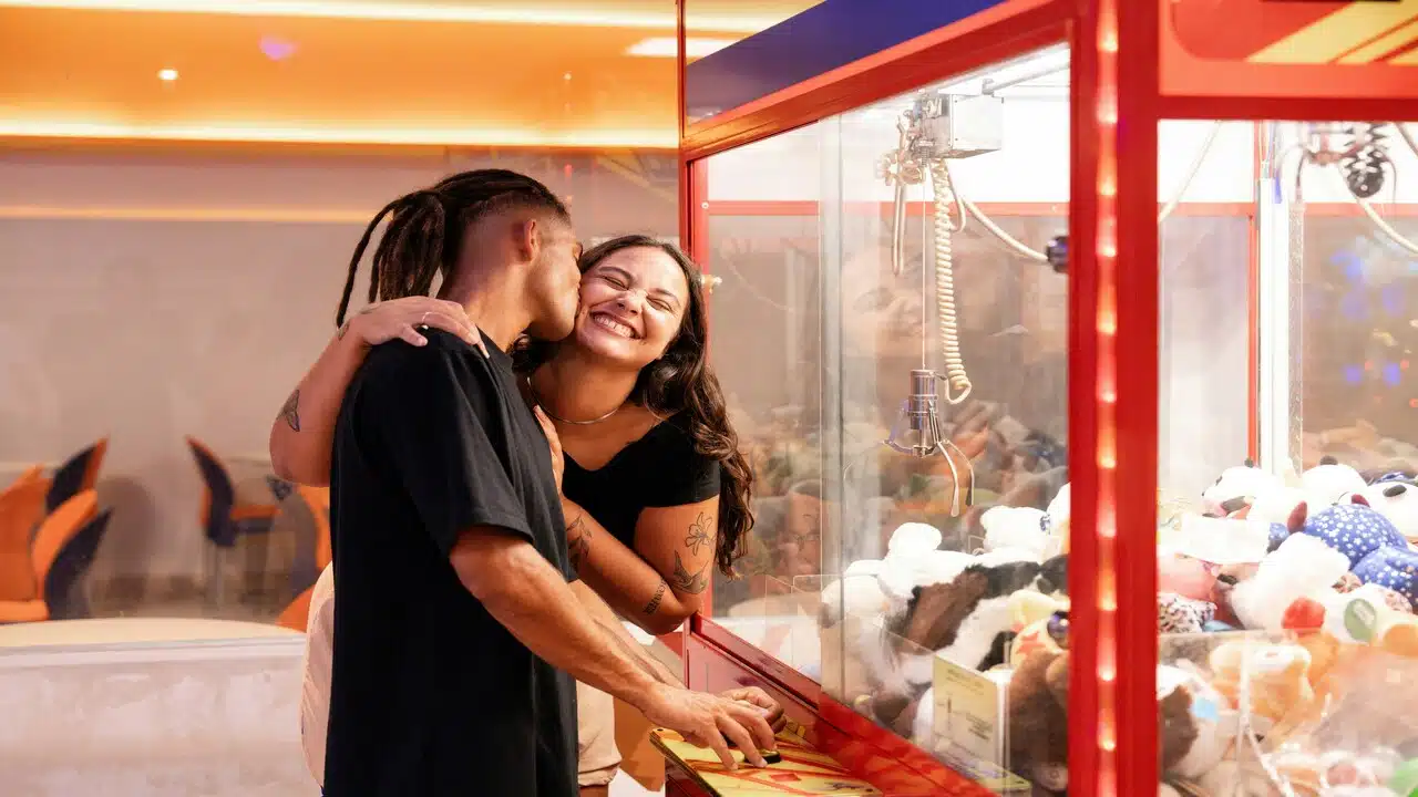 A couple clapping in front of a claw machine
