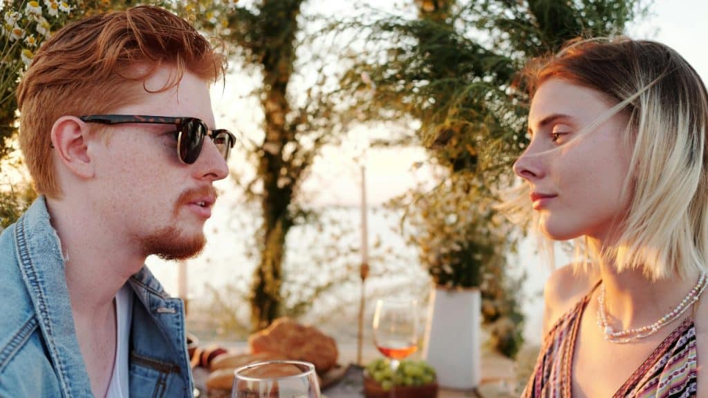 A man in sunglasses and a woman sit outdoors at a table during the sunset.