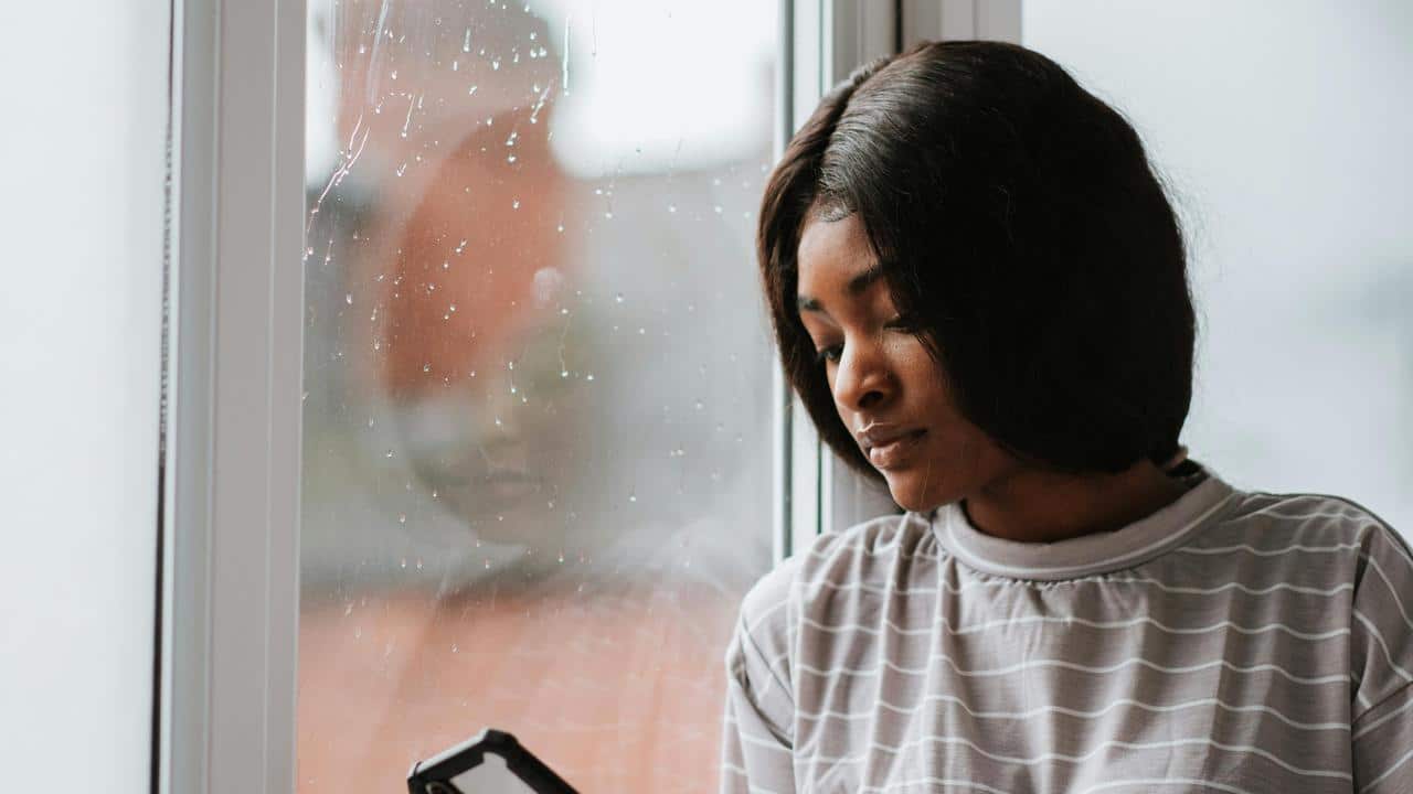 A woman looking at her phone by a rainy window.