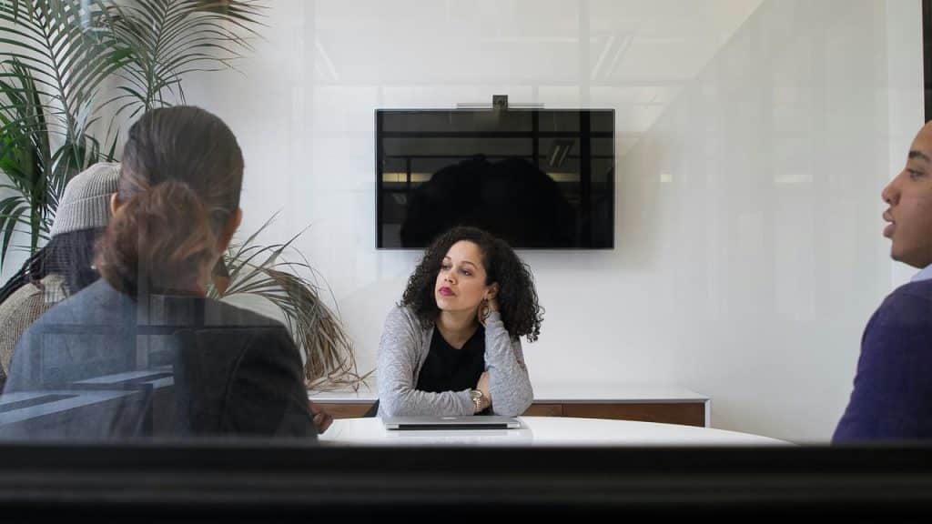A woman sits at a conference table listening during a meeting.