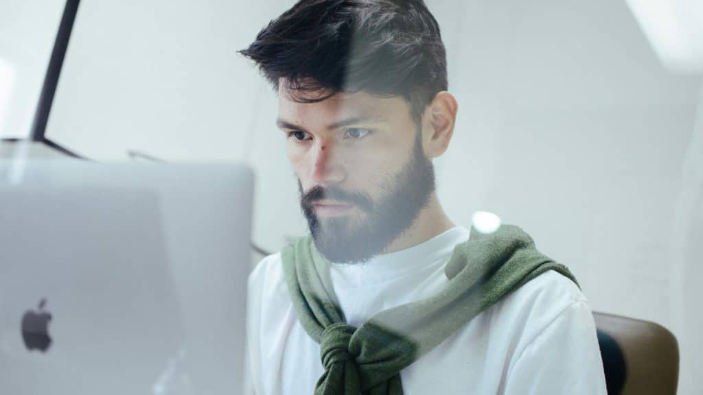 A bearded man focused on a computer screen while working indoors.