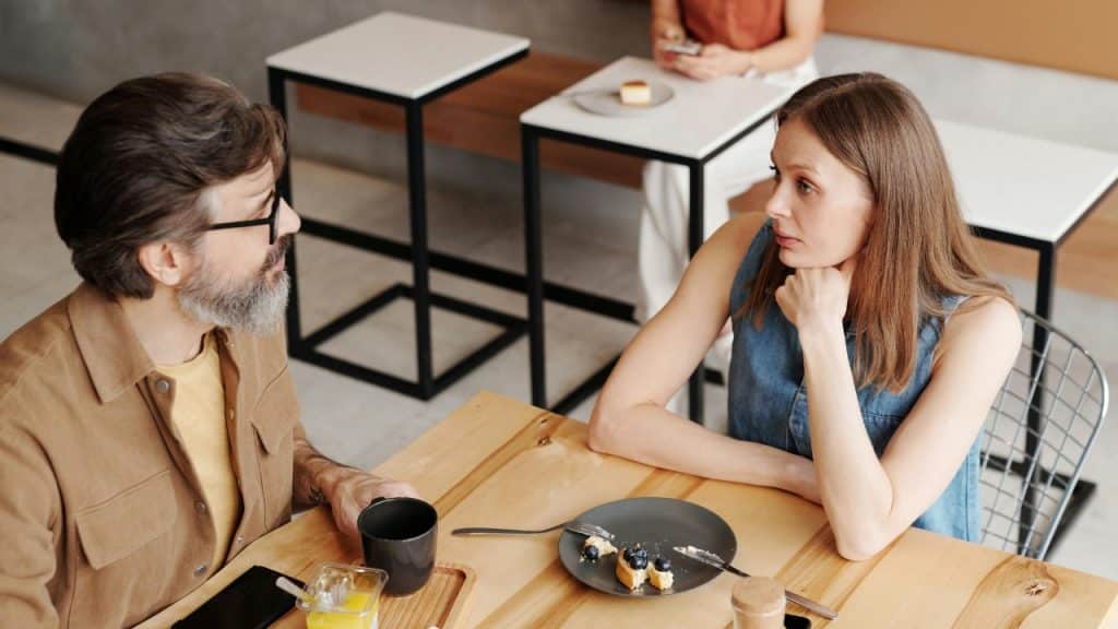 A man with a beard and a woman sitting at a wooden table in a cafe.
