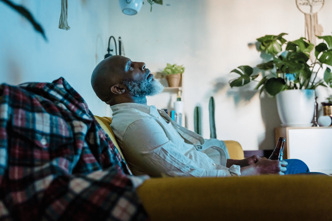 A man sitting on a sofa while drinking a beer