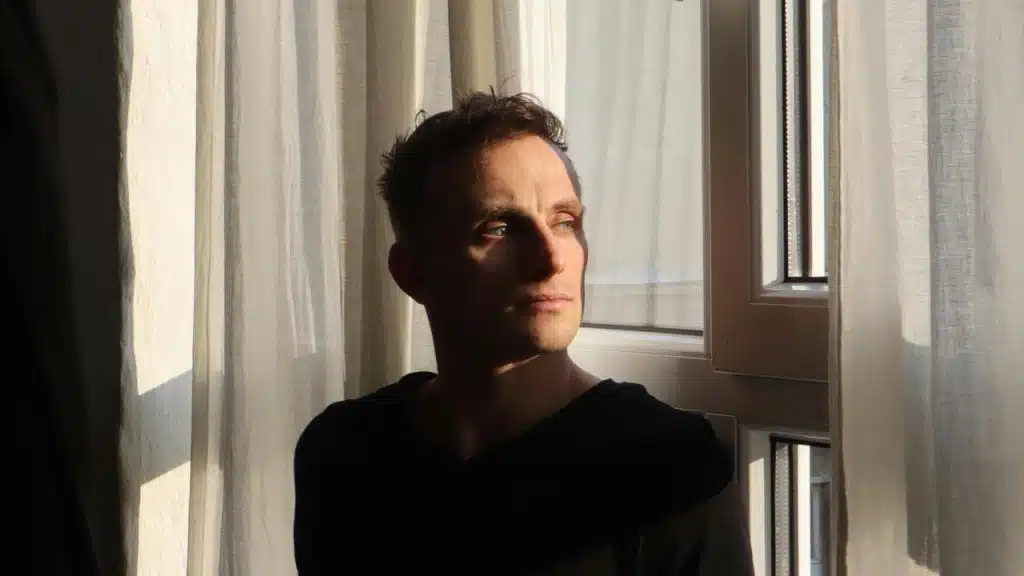 A man standing by a window with sunlight on his face.