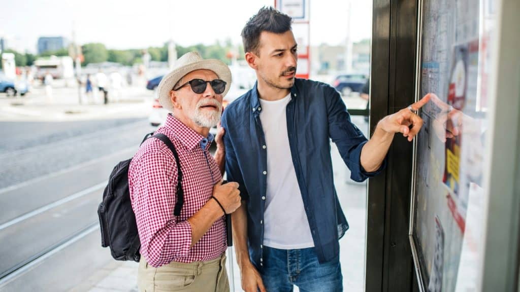 A younger man points at a map on a board for an older man.