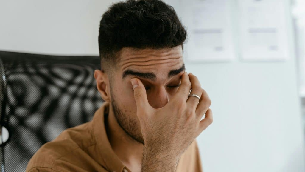 A man with a ring on his finger rubs his eyes with his hand.