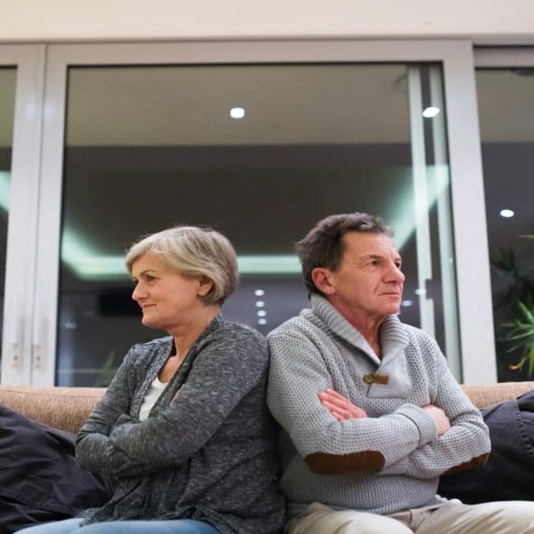 couple sitting apart on couch looking serious