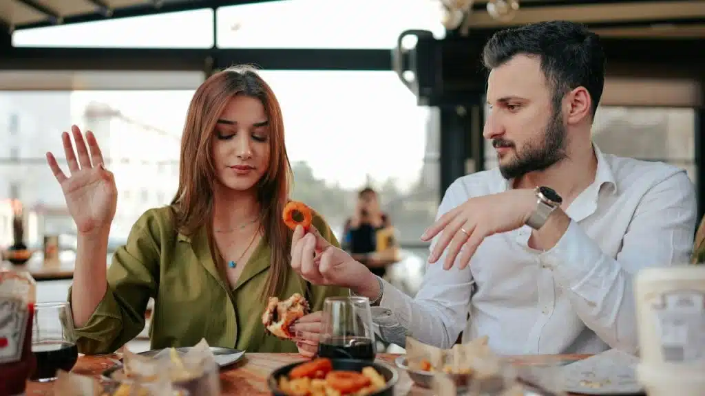 A man hands an onion ring to a woman across a restaurant table.