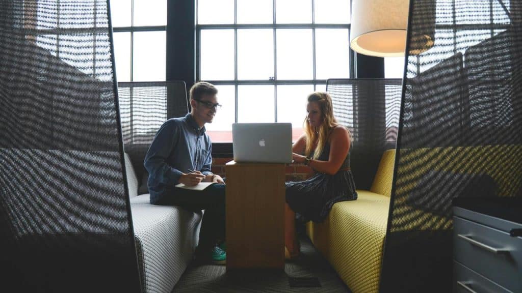 A man and woman working together on a laptop in an office booth.