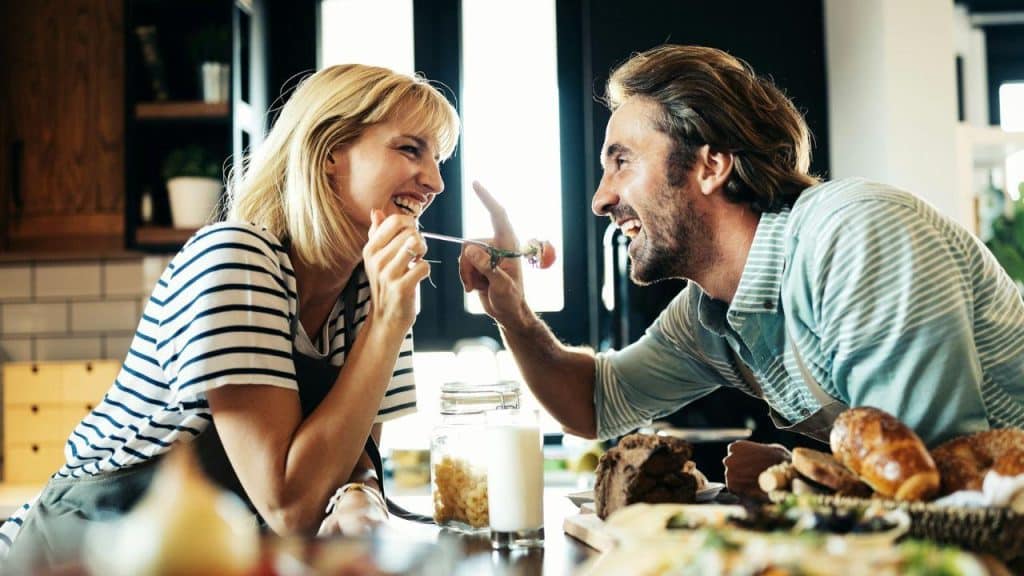 A smiling couple playfully interacts in a kitchen while preparing food.