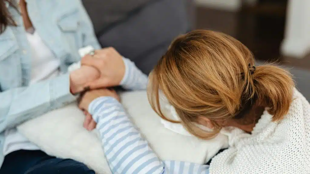 A woman rests her head on a pillow while holding someone’s hands for comfort.