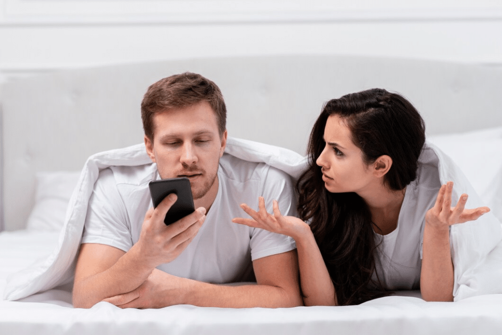 Man ignoring wife while on phone in bed