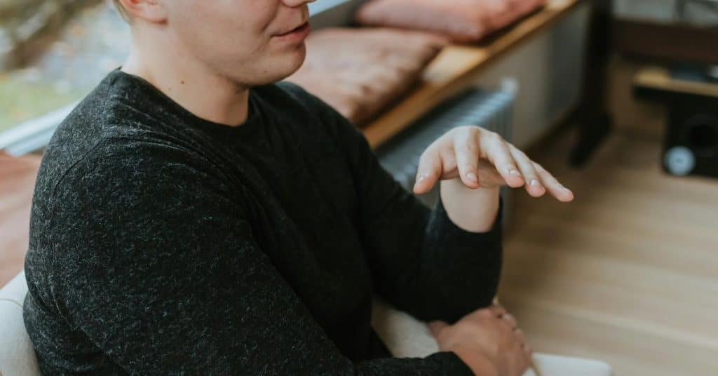 A person seated indoors gesturing with one hand while talking.