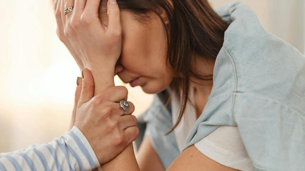 A distressed woman being comforted by another person holding her wrist.