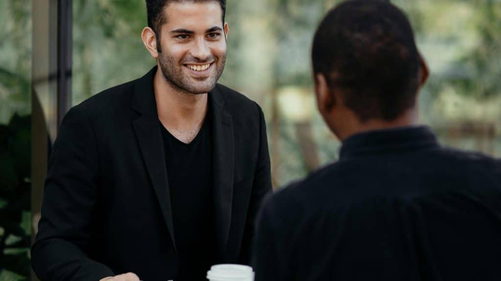 A smiling man in a blazer talking with another person at a table.
