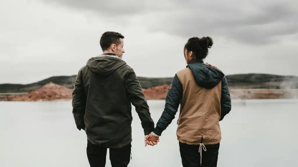 A couple holding hands in front of a lake. 