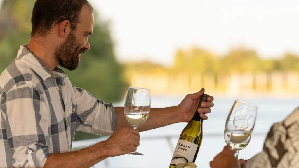 A man pouring wine into glasses while smiling outdoors.