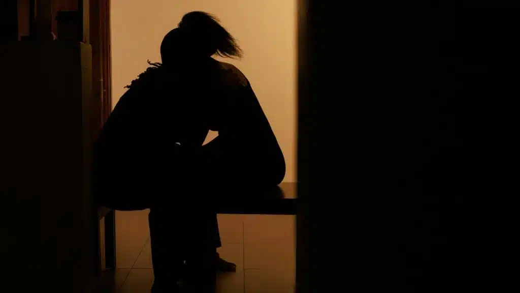 A silhouette of a person sitting alone on a bench in dim light.