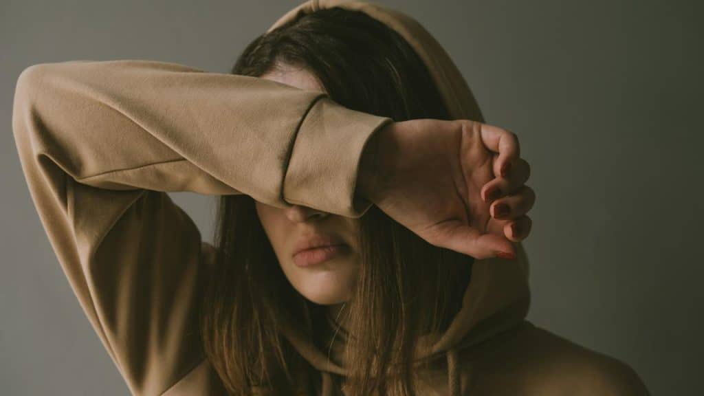 A woman in a hoodie covering her face with her arm.