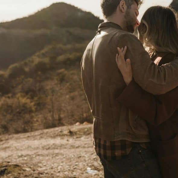 A couple embracing outdoors in a sunlit, mountainous area.
