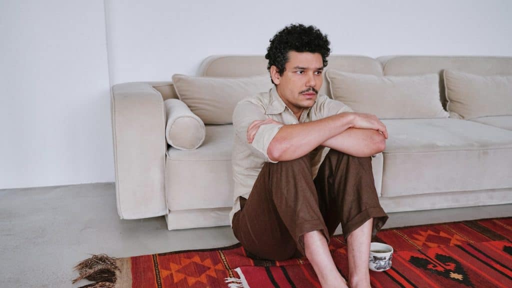 A man is sitting on a rug in front of a couch.