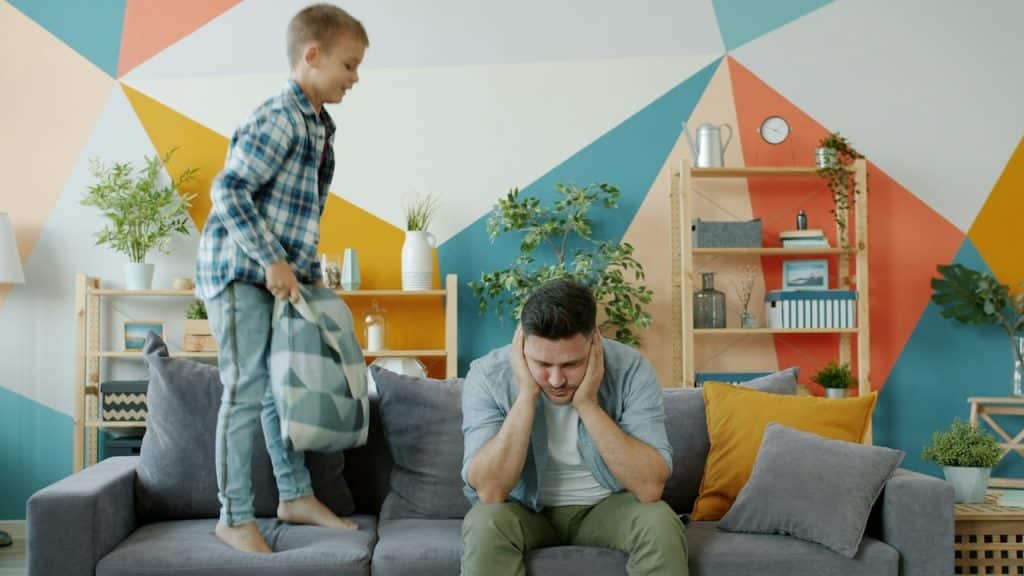 Father stressed as son jumps on couch.