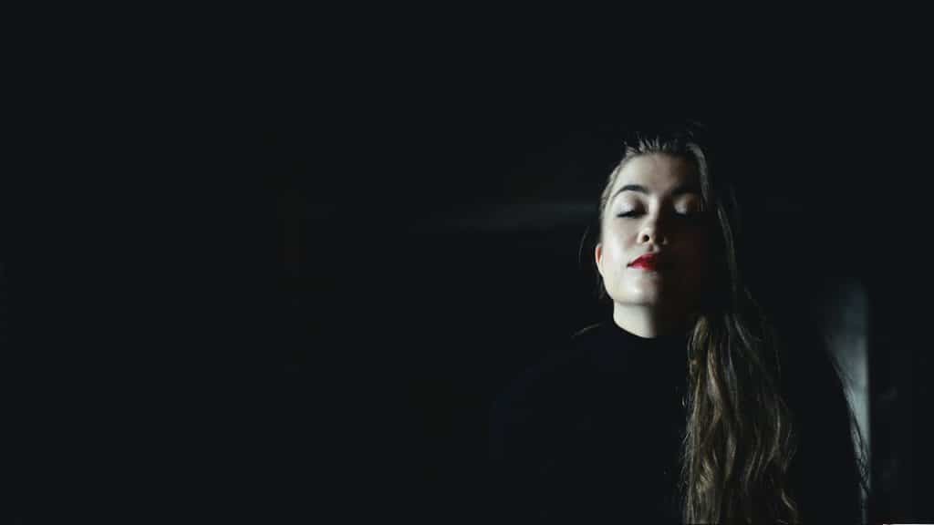 A woman wearing a black crew-neck top inside a black room.