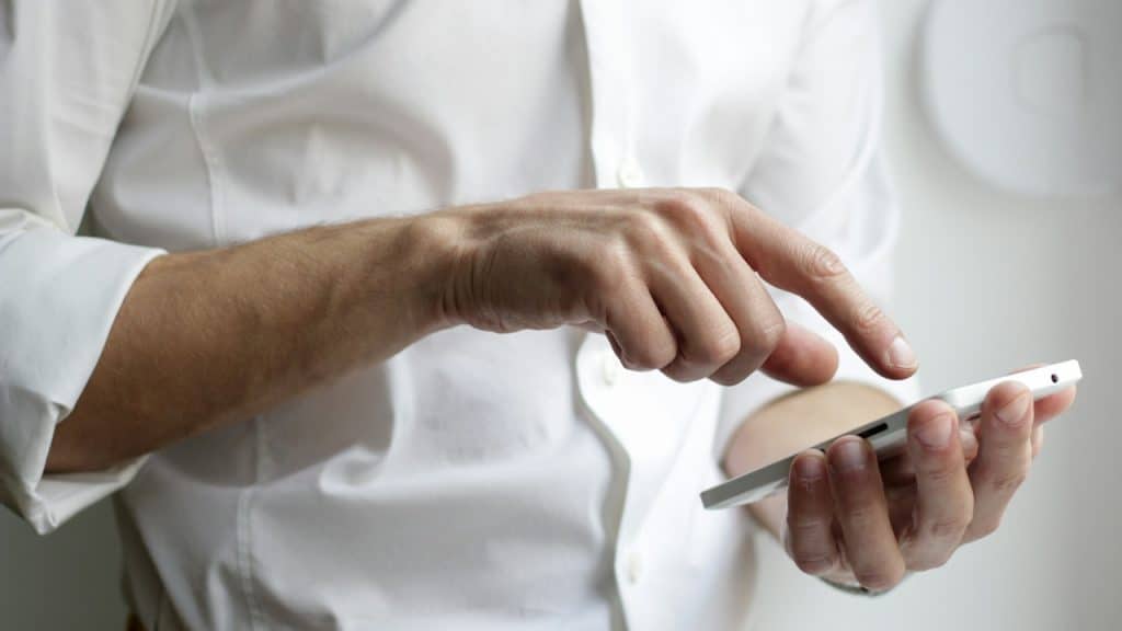 A person in a white shirt tapping the screen of a white smartphone