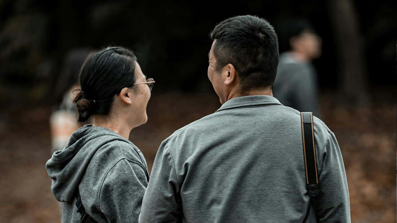 A couple standing with their backs to the camera and smiling at each other.
