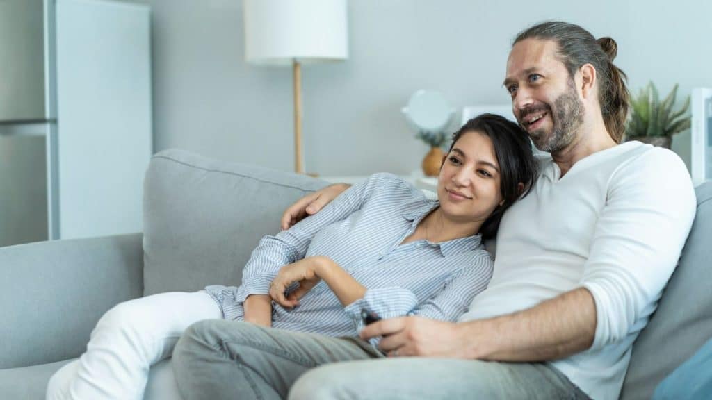 A woman leans her head on a man's shoulder as they sit together on a sofa.