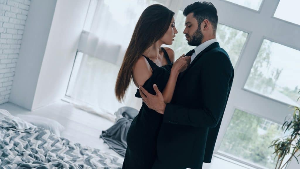 Handsome young man kissing and undressing his girlfriend while standing in the bedroom.