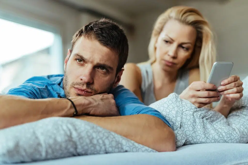 Displeased man lying on the bed and ignoring his girlfriend