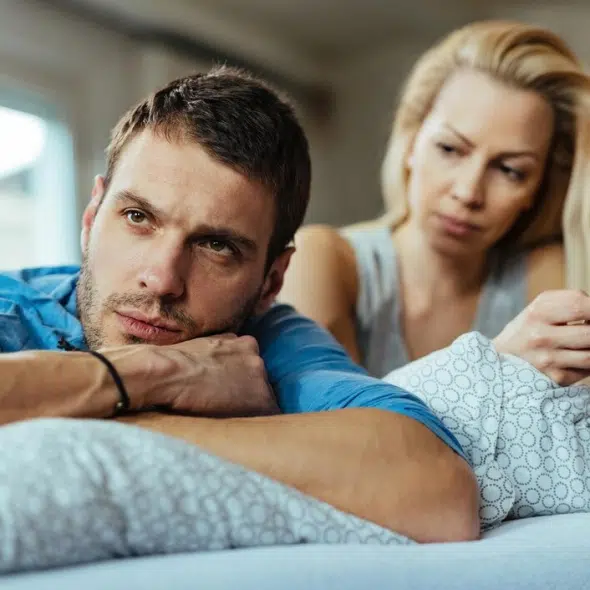 Displeased man lying on the bed and ignoring his girlfriend