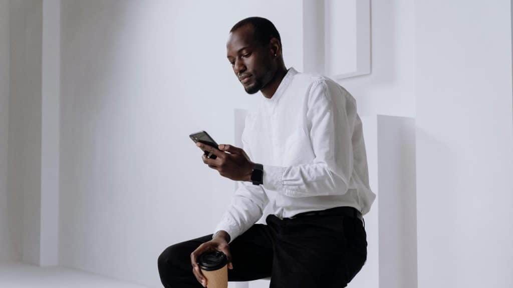 A man in a white shirt looking at his phone while holding a coffee cup.