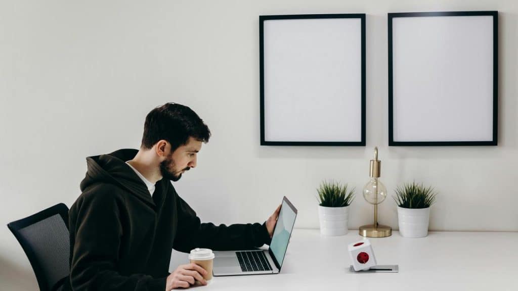 A man in a hoodie working on a laptop at a minimalist desk.