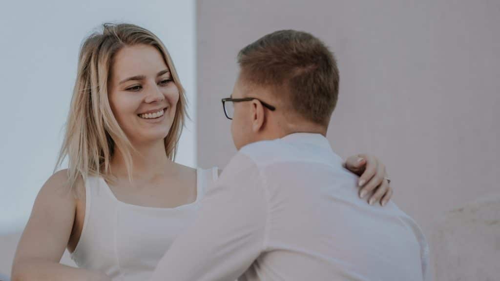 A woman in a white dress smiles while holding a man in a white shirt.