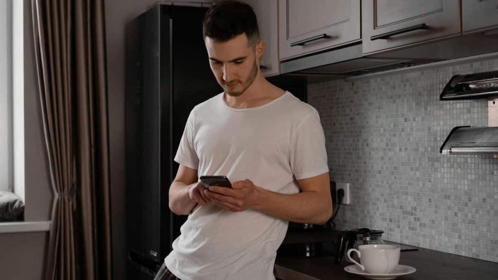 A man standing in a kitchen looking at his phone.