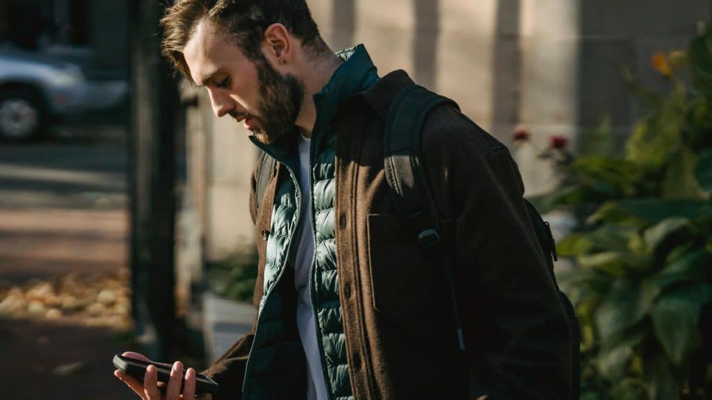 A man walking outdoors while looking at his phone.