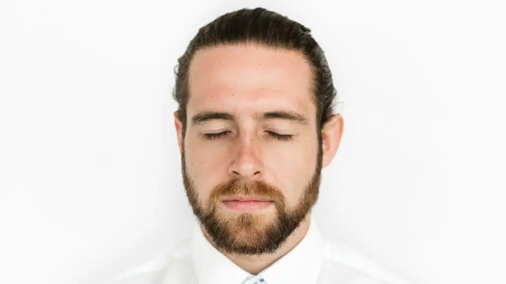 A close-up of a man with a beard, who is closing his eyes.