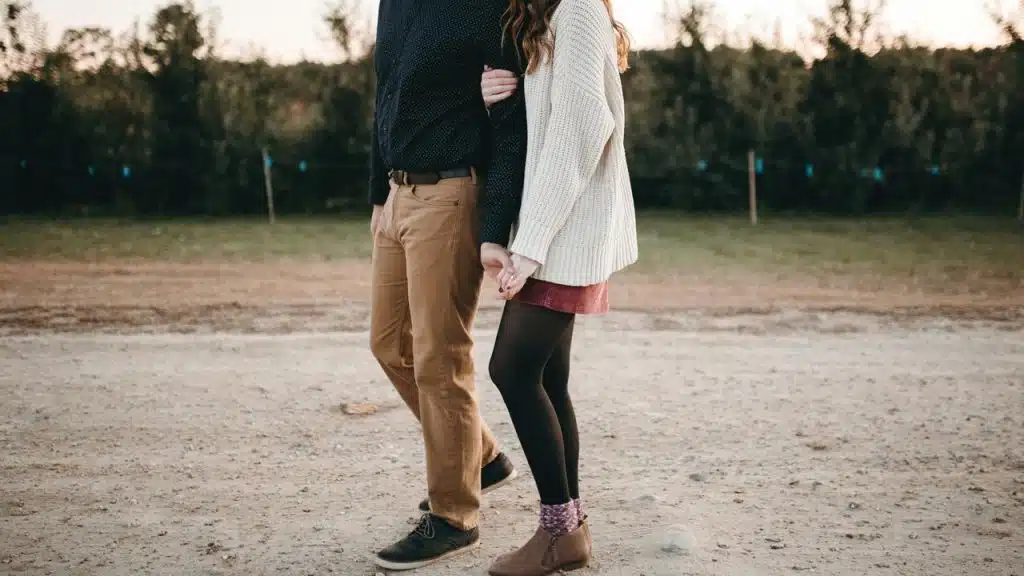 A couple holding hands while walking on a dirt path outdoors.