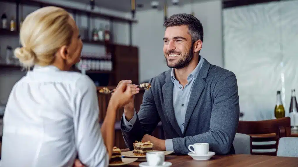 A woman feeds a piece of cake to a man as they smile at each other.