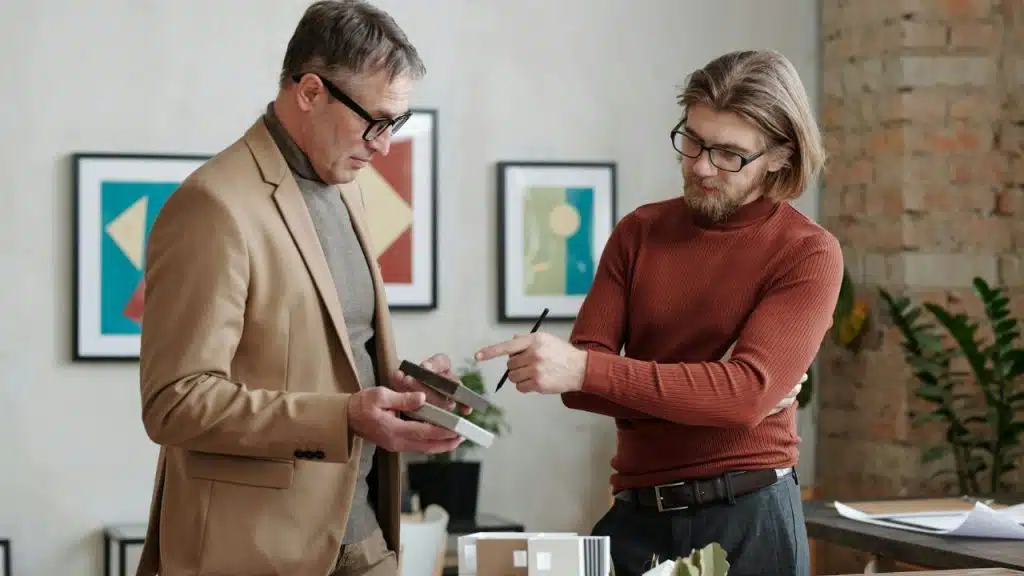 Two men in professional clothing standing together and examining small rectangular material samples.