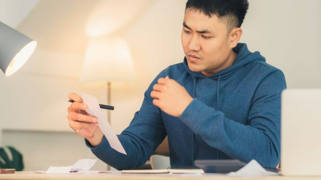 A man in a blue hoodie sits at a table examining some paperwork.