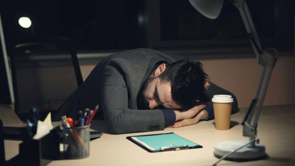 A man in a suit sleeps with his head down on a desk at night.