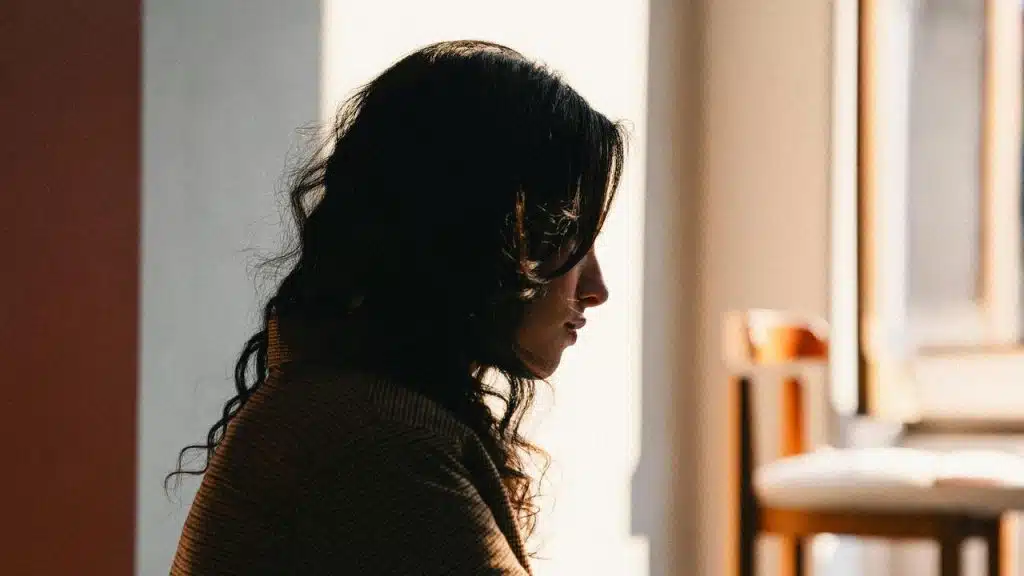 A woman sitting by a window in soft light, looking thoughtful.